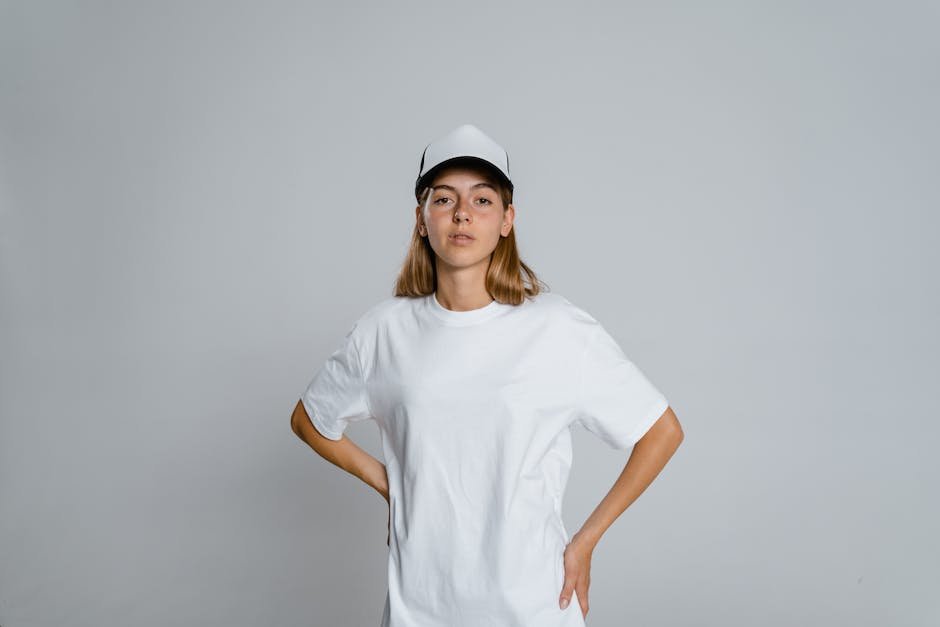 Portrait of a teenager wearing a white t-shirt and cap, standing with hands on hips.